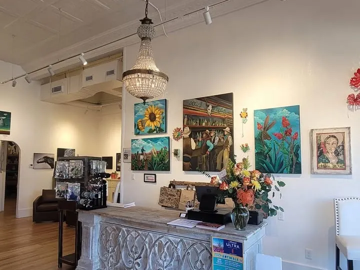 Inside 5th Street Gallery: paintings on white walls above a carved display counter, with a chandelier overhead.