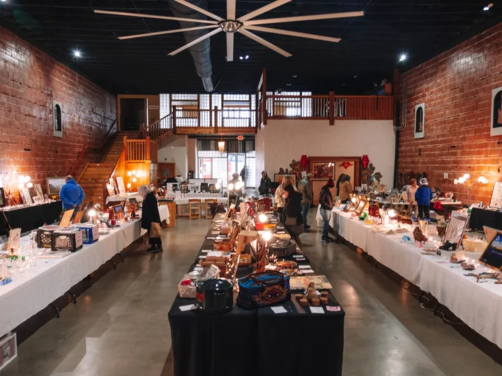 Donated art and goods on long tables in a brick-walled hall at a past Alpine Public Library silent auction.