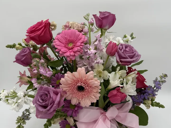 A pink and purple arrangement of roses and gerbera daisies by Paloma.